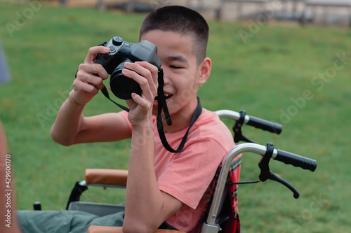 Camera in hand a special child on wheelchair is smile happy face, Hobby amateur photographer, Green nature background, Life in the education age of disabled children, Happy disability kid concept.