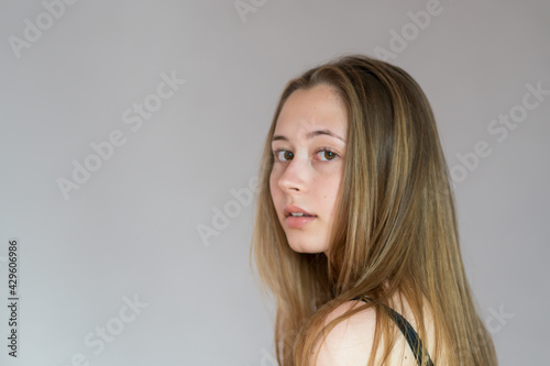 Close up studio portrait of a young back turned woman turning her head looking at the camera. Grey background