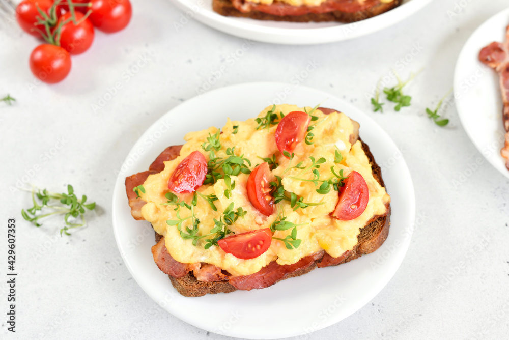 Scrambled eggs with microgreen, bacon and tomato slices on bread