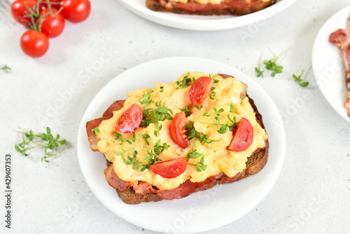 Scrambled eggs with microgreen, bacon and tomato slices on bread