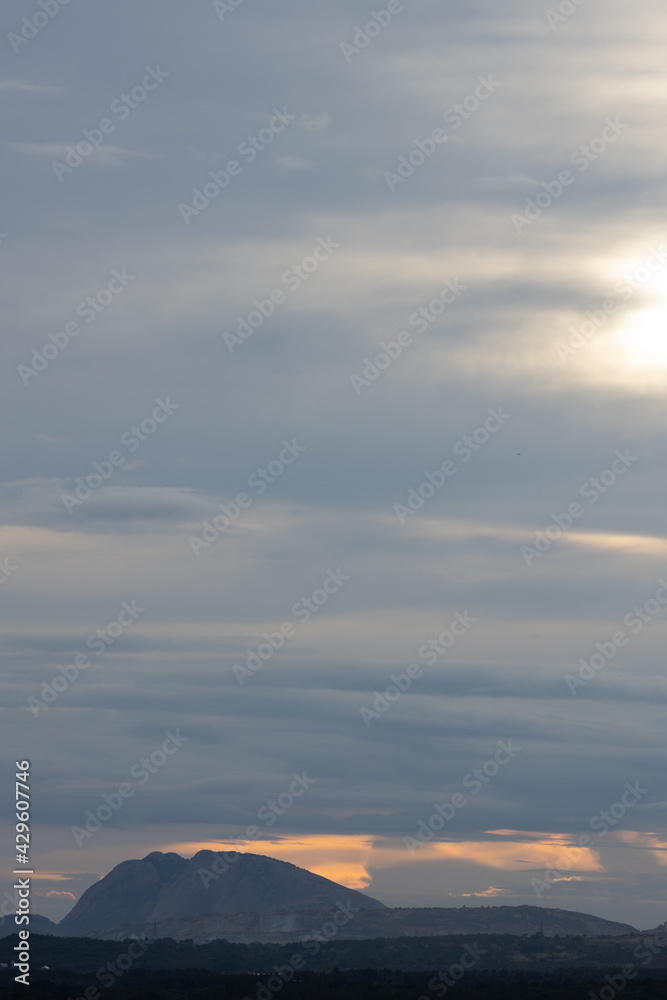 Silhouette of a hill at the bottom and dark clouds in the horizon with a streak of yellow light in between
