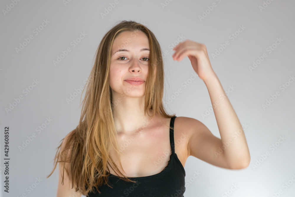Studio portrait of a young blonde woman adjusting her hair with her hand Studio portrait of a young blonde woman adjusting her hair with her hand