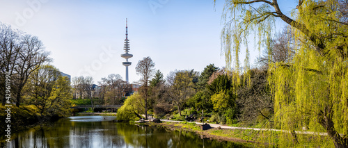 horizontal wide angle panorama view from old main entrance of planten un blomen garden in the wallgraben to the famous heinrich-hertz television tower in the middle of hamburg, germany