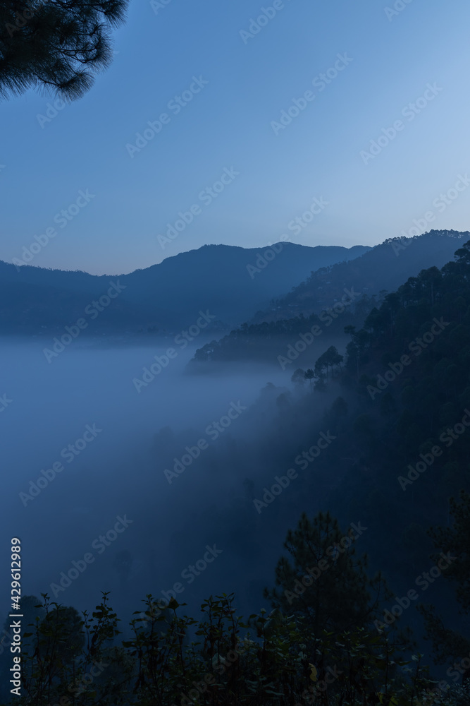 Layers of mountains with pine trees on them and fog and mist  settled in the valley 