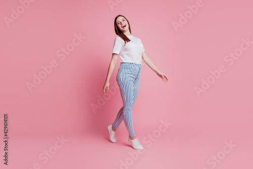 Charming carefree lady walk look camera on pink background wear casual outfit © Tetiana