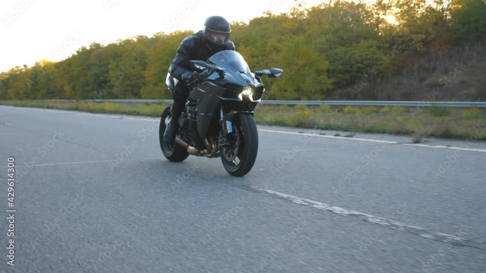 Young man in helmet riding on modern sport motorbike at highway with sun flare at background. Motorcyclist racing his motorcycle on country road. Guy driving bike during trip. Concept of freedom Young man in helmet riding on modern sport motorbike at highway with sun flare at background. Motorcyclist racing his motorcycle on country road. Guy driving bike during trip. Concept of freedom