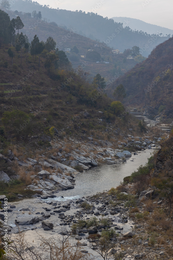 A river flowing through a narrow valley with stones and rocks scattered and mountain ranges with sky in the horizon
