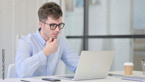 Young Man with Laptop Thinking at Work 