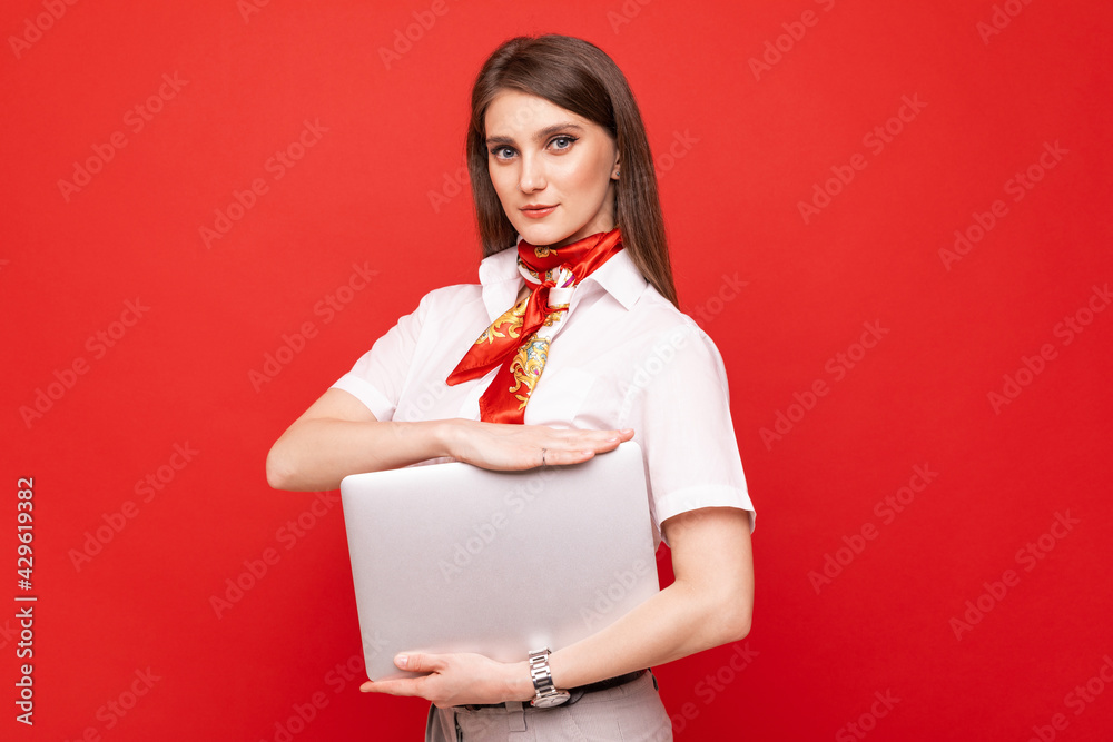 Portrait of a young woman in a white shirt holding a laptop on a red background