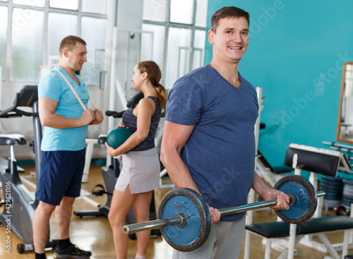 Sporty man doing strength exercises with barbell in gym