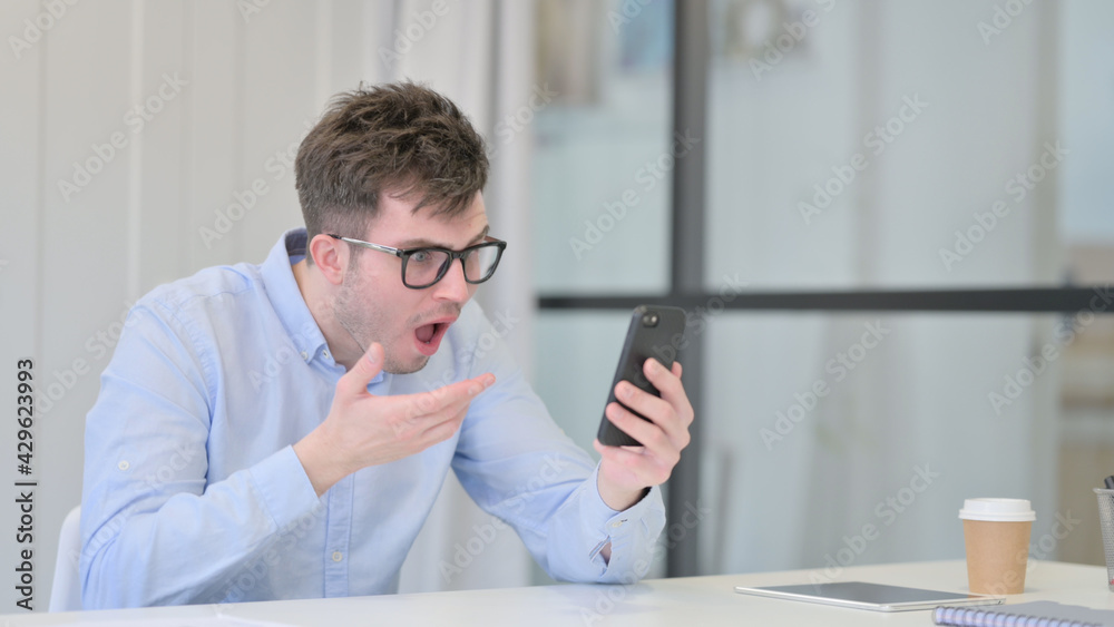 Young Man Reacting to Loss on Smartphone in Office Young Man Reacting to Loss on Smartphone in Office