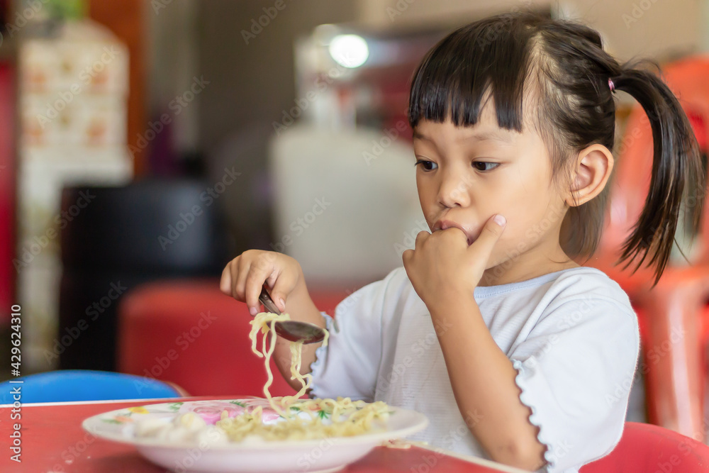Portrait​ image​ of​ 2-3 yeas​ old​ of​ baby.​ Happy​ Asian child girl eating and biting the noodle. Enjoy eating moment. Healthy food and kid concept.​ Sucking fingers in the mouth.
