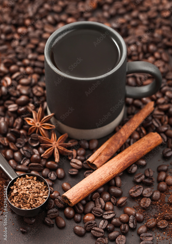 Fototapeta premium Black coffee in tall cup with anise star and cinnamon on ground coffee and beans with coffee scoop