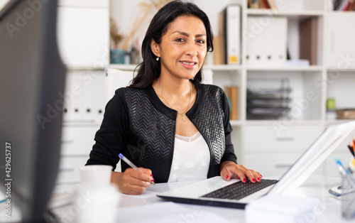 Photography Smiling successful hispanic business woman working on laptop in modern office