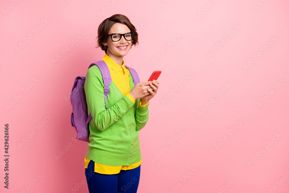 Photo of cute young lady dressed yellow shirt glasses backpack holding modern device empty space isolated pink color background Photo of cute young lady dressed yellow shirt glasses backpack holding modern device empty space isolated pink color background
