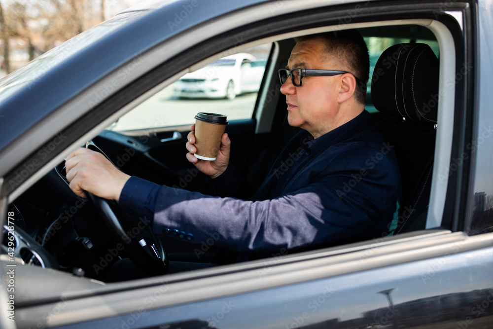 Drinking on the go. Handsome middle age man sitting on the drivers seat of his car and drinking his morning coffee. Drinking on the go. Handsome middle age man sitting on the drivers seat of his car and drinking his morning coffee.