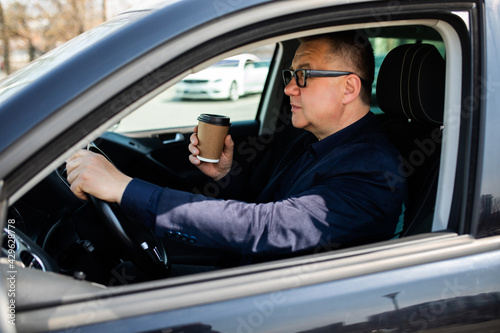 Drinking on the go. Handsome middle age man sitting on the drivers seat of his car and drinking his morning coffee. © F8  \ Suport Ukraine