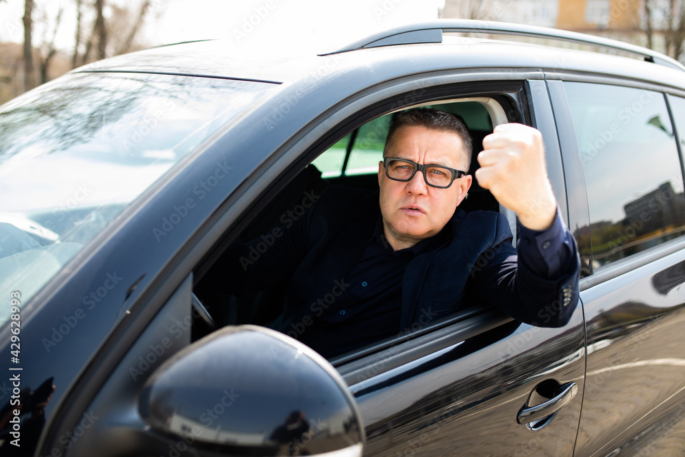 Angry man looking outside from car window with fist up Angry man looking outside from car window with fist up