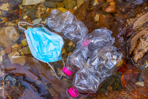 Masks and plastic bottles thrown into the waters of a stream.  photo
