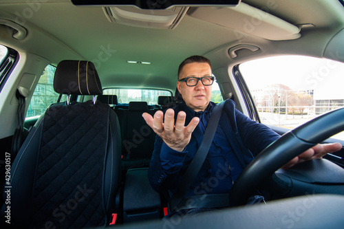 Adult middle age man in a traffic jam, loosing his tamper and showing with his hand on something