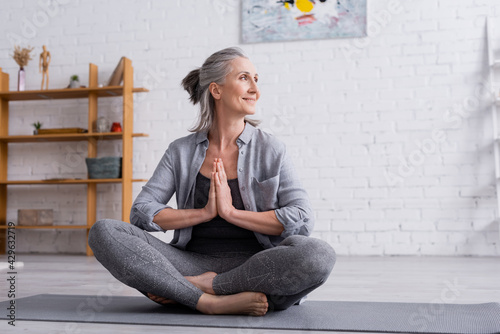 happy mature woman with grey hair sitting with praying hands in lotus pose on yoga mat photo