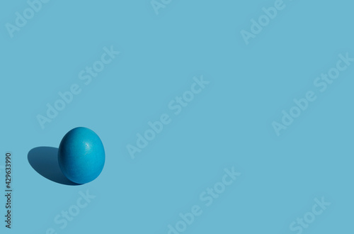 A blue Easter egg with a hard shadow on a blue background. Copy space. The concept of minimalism.