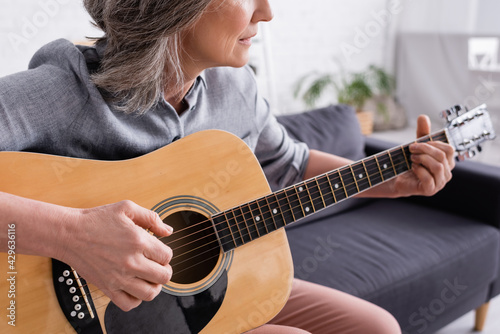 cropped view of middle aged woman with grey hair playing acoustic guitar