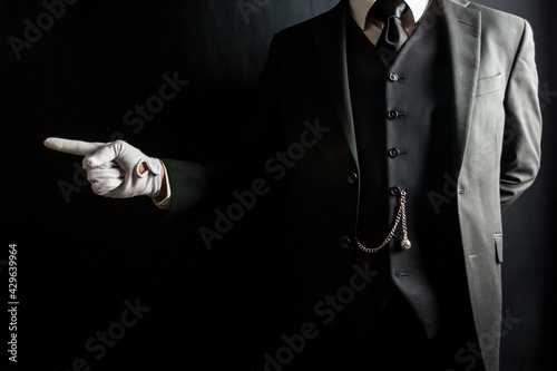 Portrait of Butler or Servant in Dark Suit and White Gloves Pointing the Way. Concept of Service Industry and Professional Hospitality.