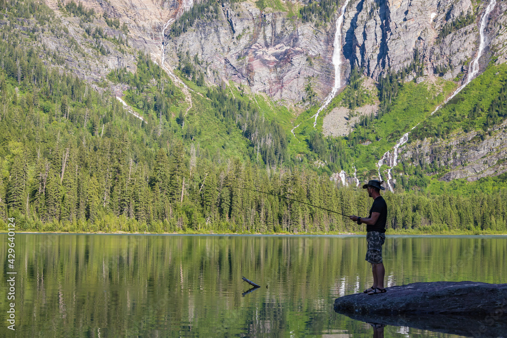 Fisherman showing off his catch at Avalanche Lake and surrounding mountain range at Glacier National Park