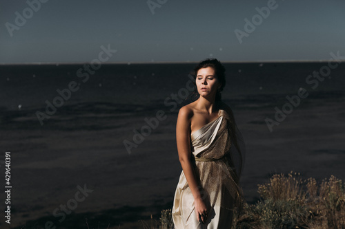 A beautiful girl in a stilted suit stands on a mountain above the sea, a lake on a sunny day.