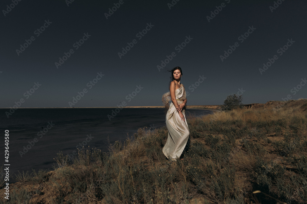 A beautiful girl in a stilted suit stands on a mountain above the sea, a lake on a sunny day.