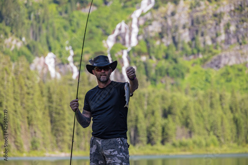 Fisherman showing off his catch at Avalanche Lake and surrounding mountain range at Glacier National Park