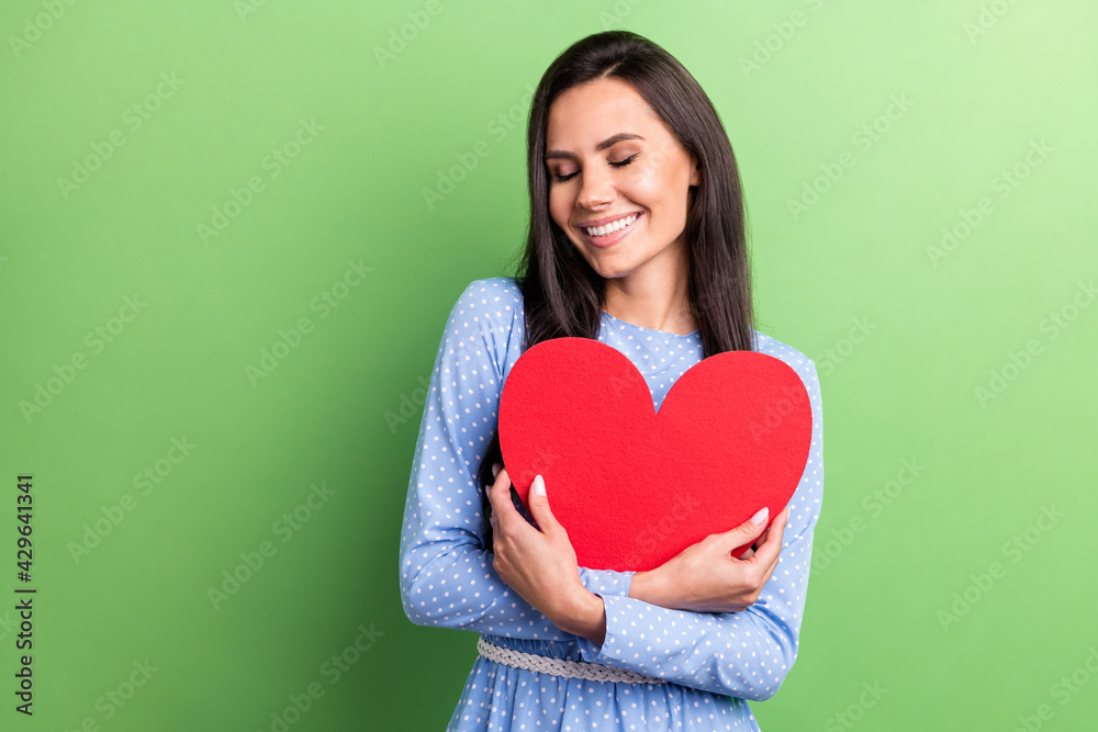 Photo of cute dreamy young lady wear dotted clothes smiling hugging red heart isolated green color background Photo of cute dreamy young lady wear dotted clothes smiling hugging red heart isolated green color background