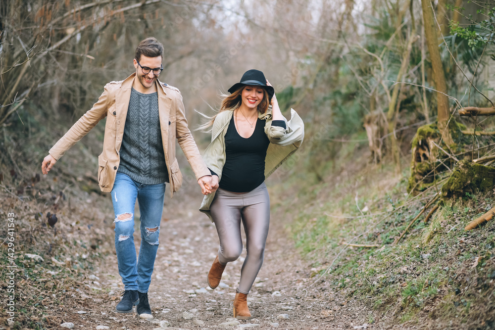 Young pregnant couple running outdoor having fun together in nature