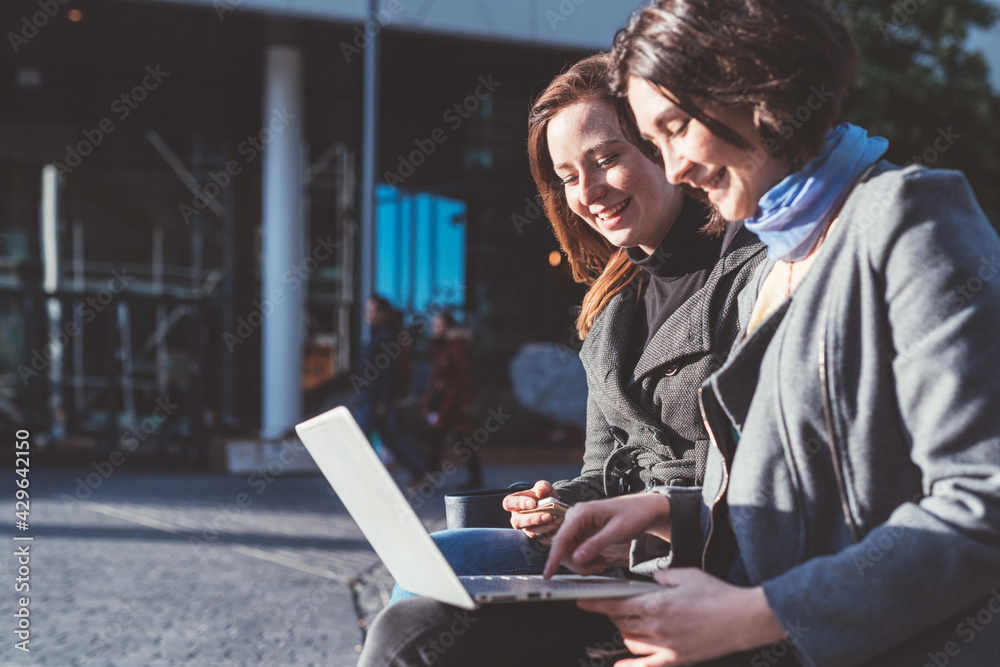 two young women sitting outdoor using notebook two young women sitting outdoor using notebook
