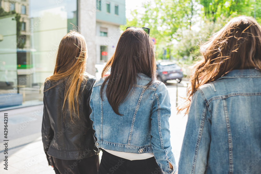 Back view of three young beautiful caucasian millennials women walking outdoor in the city