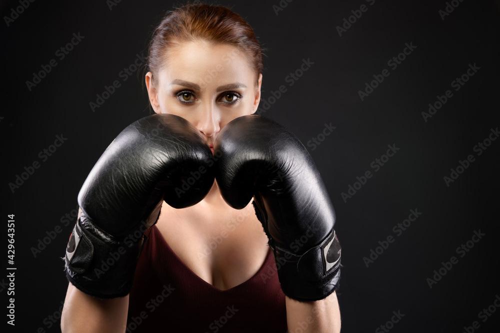 Portrait Caucasian fitness girl in boxing gloves stands in a rack on a black background, portrait of a strong and independent woman fighter