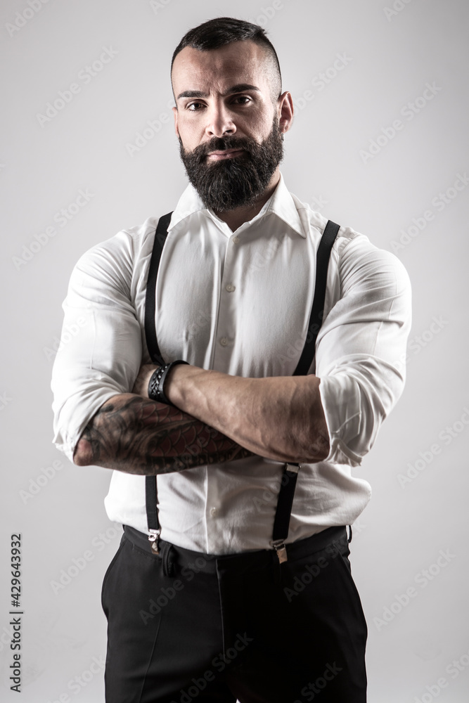 Uomo moro con la barba con camicia bianca e bretelle nere, incrocia le  braccia con espressione seria, isolato su sfondo Stock Photo | Adobe Stock