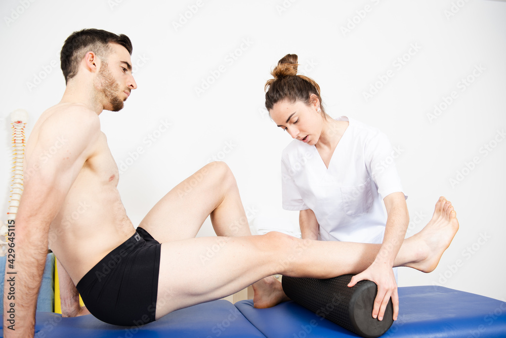Physiotherapist relaxing the calf muscle of an athlete using a foam roller. Physiotherapist relaxing the calf muscle of an athlete using a foam roller.