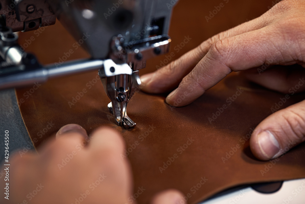 Working process of leather craftsman. Tanner or skinner sews leather on a special sewing machine, close up.worker sewing on the sewing machine Working process of leather craftsman. Tanner or skinner sews leather on a special sewing machine, close up.worker sewing on the sewing machine