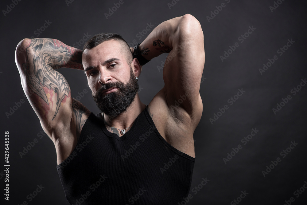 Uomo moro muscoloso, tatuato con la barba, isolato su sfondo nero