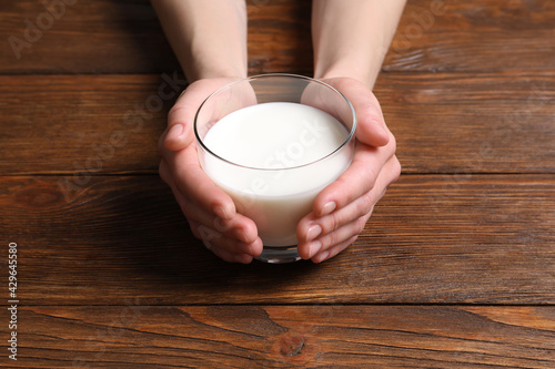 Woman holding glass of milk at wooden table, closeup