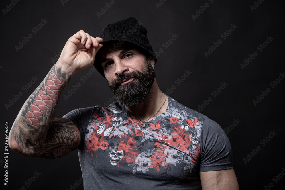 Uomo moro muscoloso con maglietta color fantasia si mette apposto il cappellino , isolato su sfondo nero
