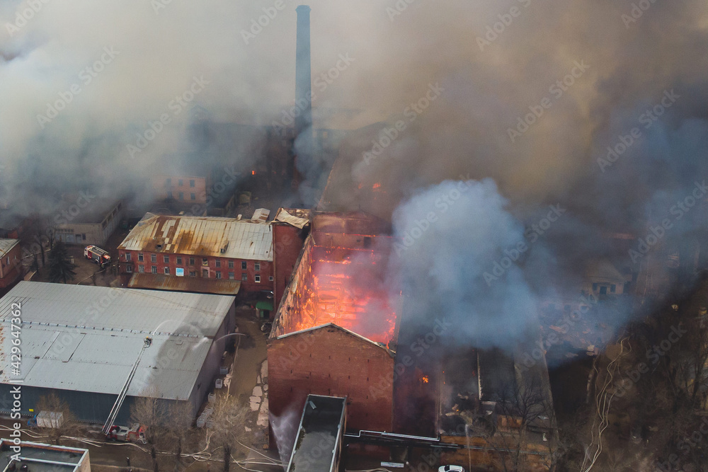 Massive large blaze fire in the city, aerial drone top view brick factory building on fire, hell major fire explosion flame blast,  with firefighters team, arson, burning house damage destruction