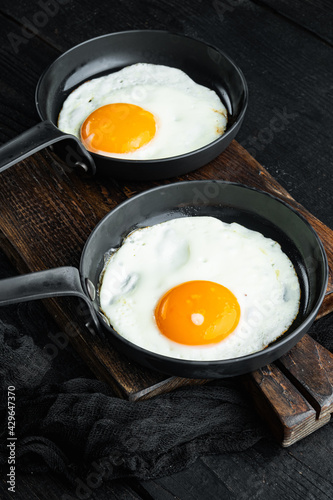 Scrambled eggs in frying pan with pork lard, bread and green feathers in cast iron frying pan, on black wooden table background