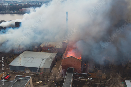 Massive large blaze fire in the city, aerial drone top view brick factory building on fire, hell major fire explosion flame blast, with firefighters team, arson, burning house damage destruction