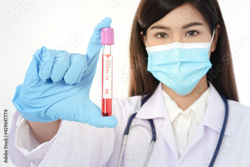An Asian female doctor wearing a blue mask holds a test tube  vaccine  sample  against the coronavirus.  COVID-19 . Hospital medical service concept. Antiviral vaccine.