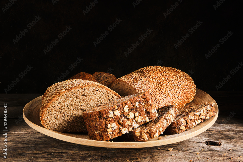 Sliced cereal bread and bread sprinkled with sesame seeds in a round plate.