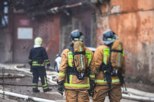Firefighters put out large massive fire blaze, group of fire men in uniform during fire fighting operation in the city streets, firefighters with the fire engine truck fighting vehicle