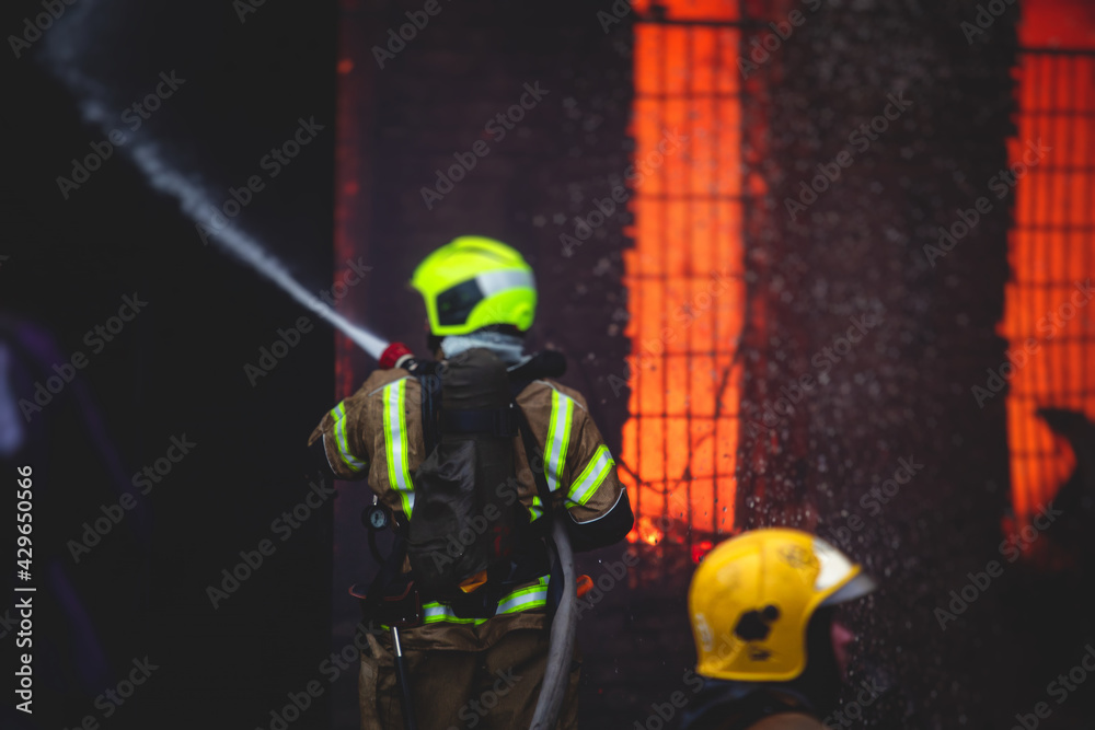 Fototapeta premium Firefighters put out large massive fire blaze, group of fire men in uniform during fire fighting operation in the city streets, firefighters with the fire engine truck fighting vehicle